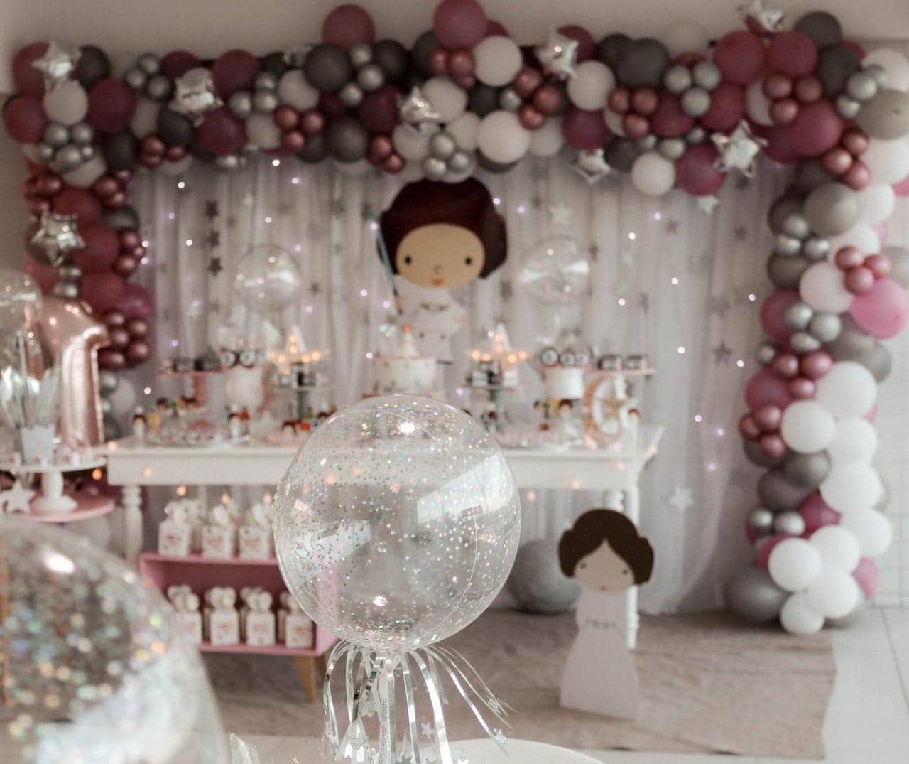 Mesa de festa decorada com arco de balões, bolo e doces